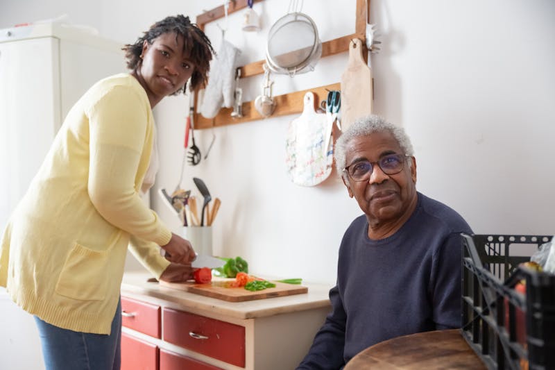 A caregiver assisting an elderly person with meal preparation in a home kitchen