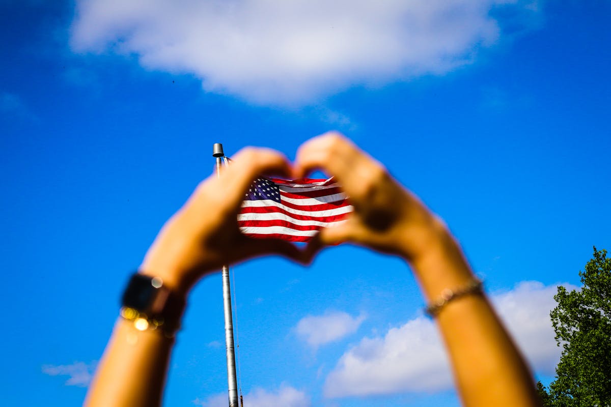 Hands forming a heart around an American flag against a blue sky — representing family gratitude and the care veterans have earned