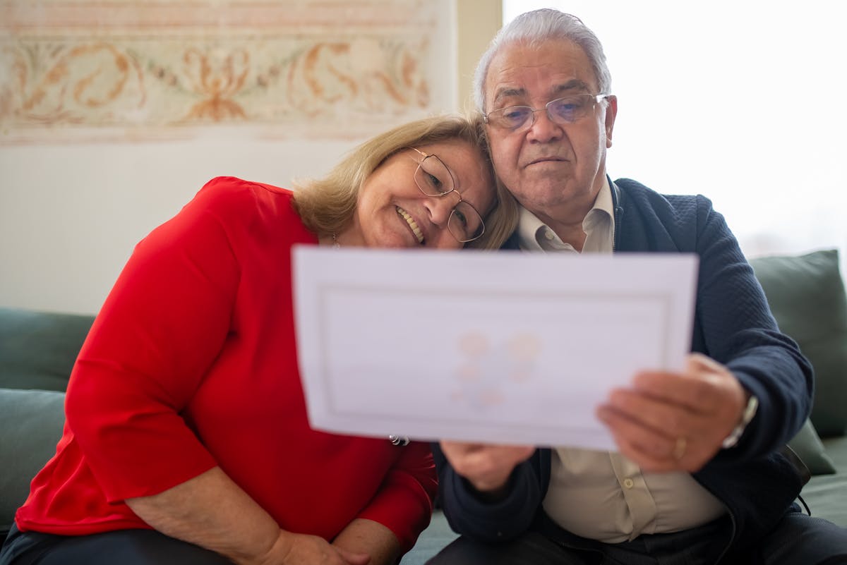 Senior couple carefully reviewing Medi-Cal yellow envelope renewal paperwork together on couch