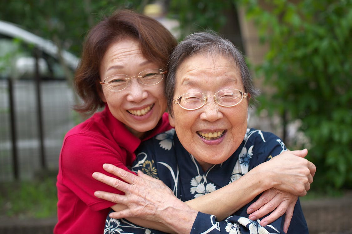 Elderly woman and adult daughter sharing a warm embrace outdoors in natural light