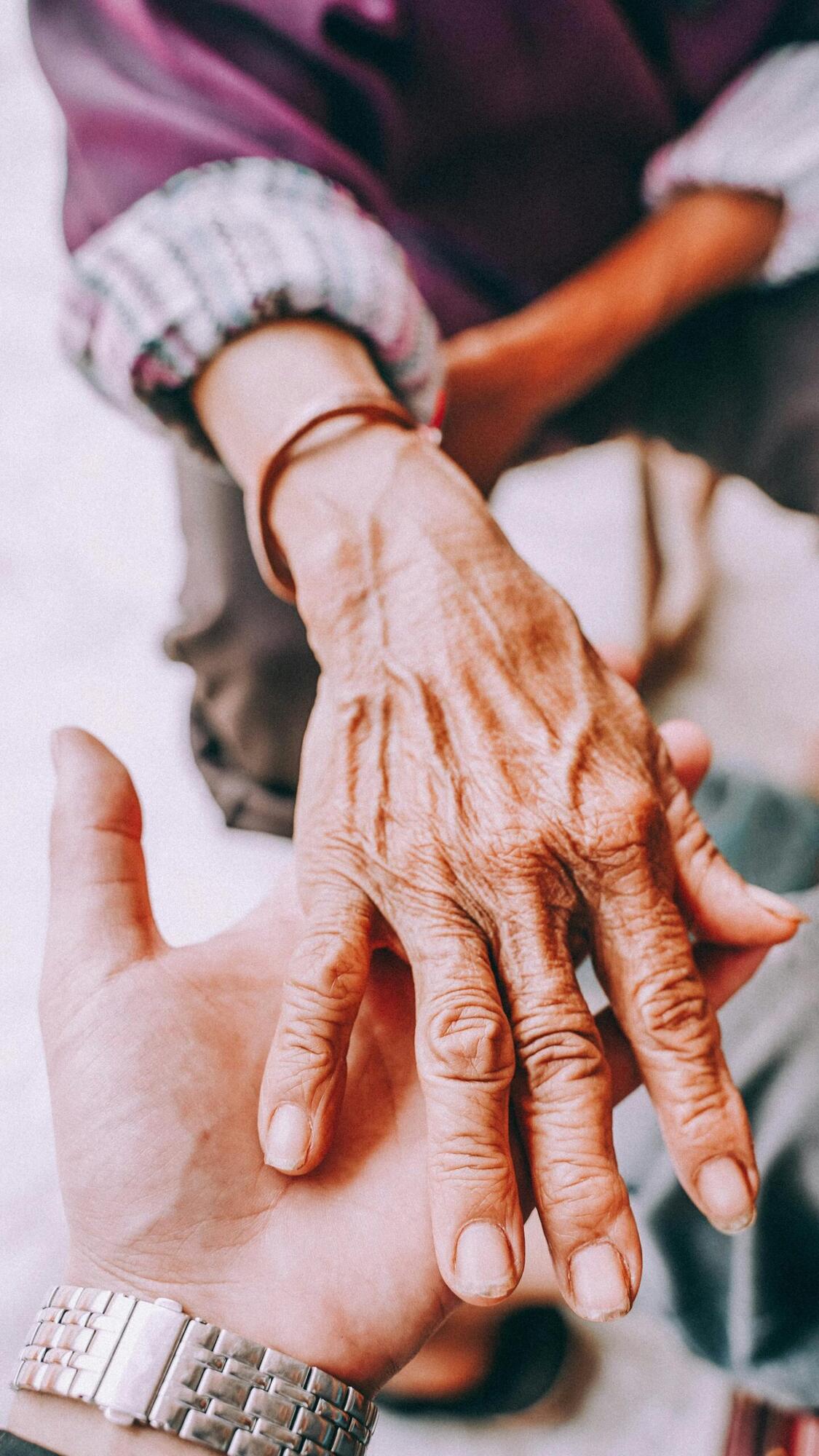 Younger hand holding the hand of a senior — symbol of the GUIDE caregiver respite benefit