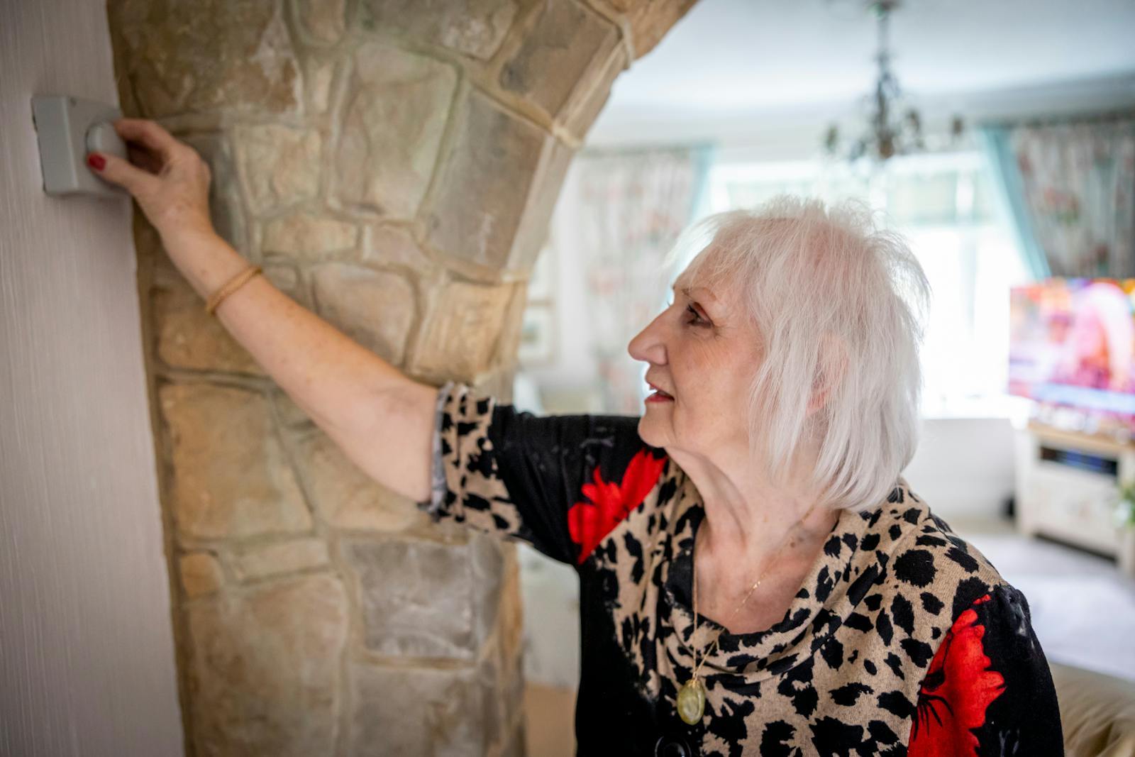 Elderly woman adjusting indoor thermostat for cooler temperature during heat wave