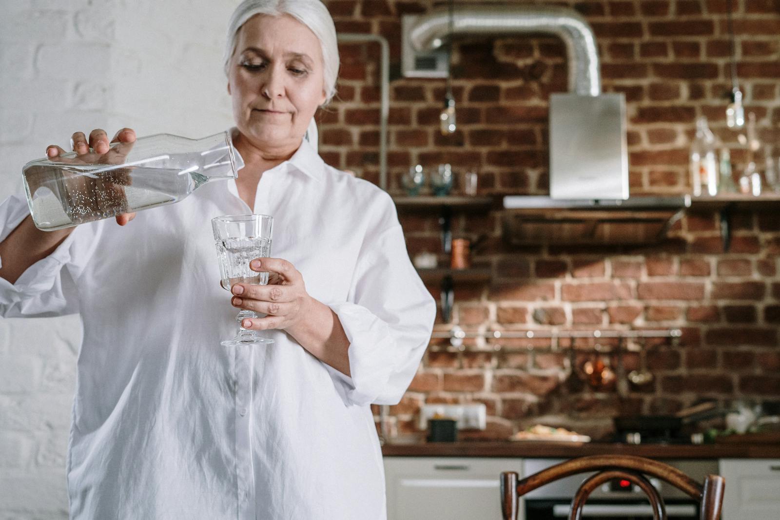 Elderly woman pouring a glass of water at home — proactive hydration during the OC heat wave