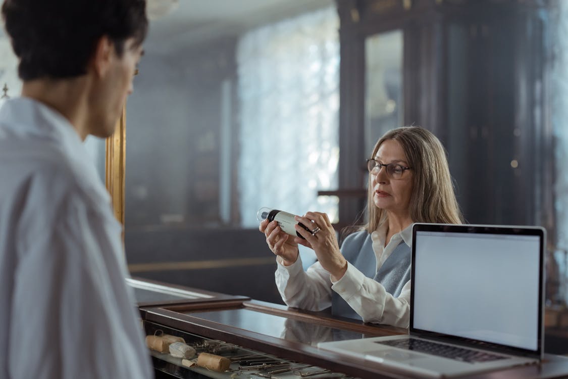 Elderly woman with eyeglasses reviewing a medication bottle at home — understanding which drugs raise heat risk is a critical caregiver step