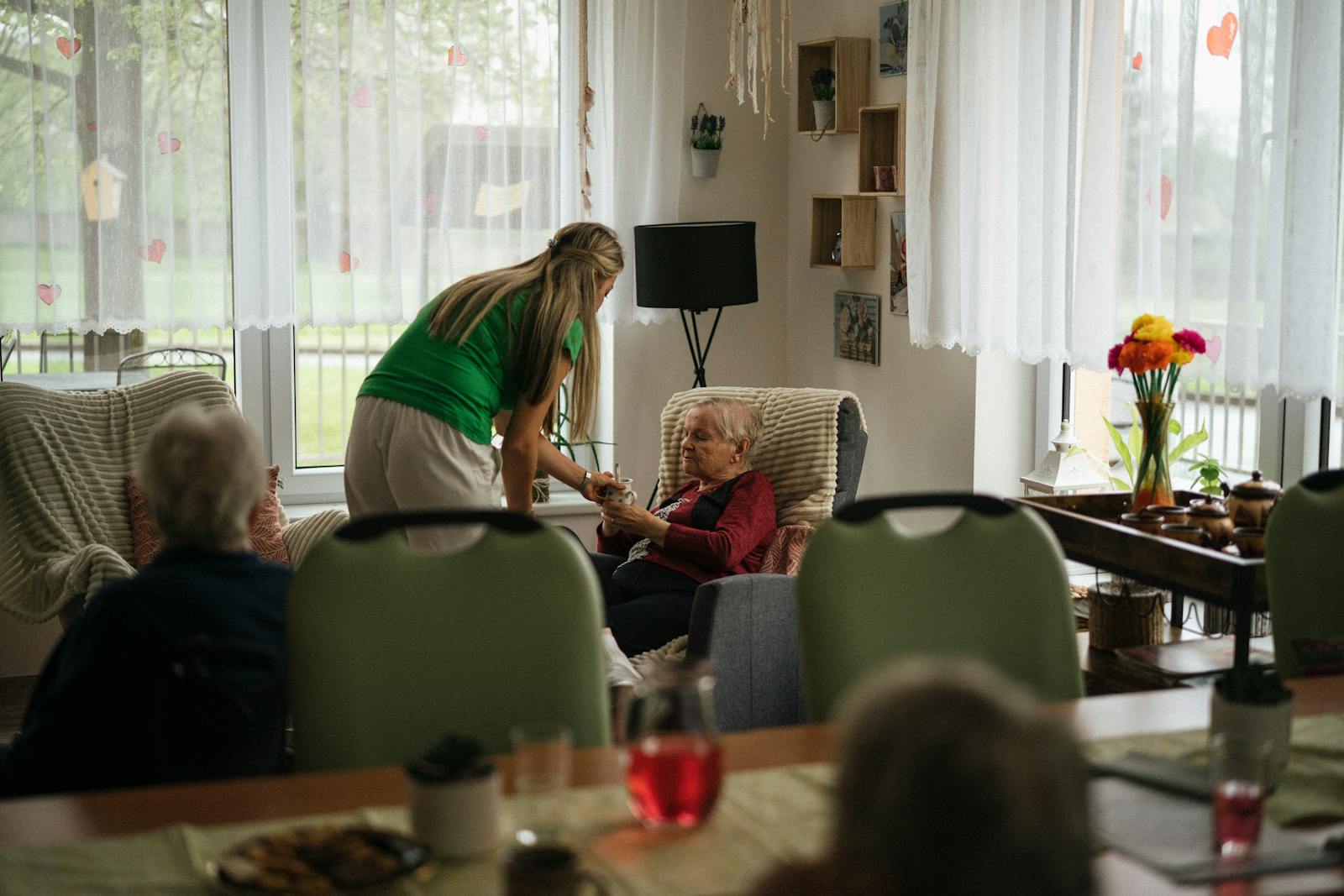 Caregiver checking on an elderly woman seated in a bright living room during a summer wellness visit in Orange County