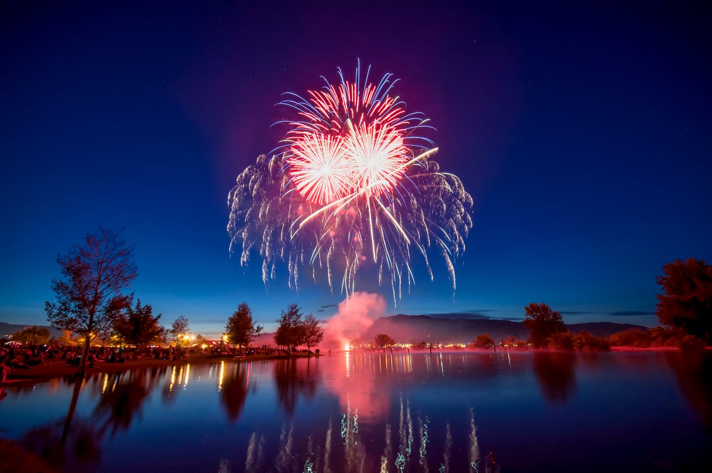 Colorful red and blue fireworks display reflecting over a lake at night during Independence Day celebrations