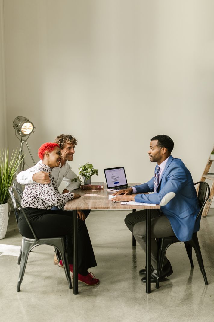 A financial advisor reviewing documents on a laptop with a couple across a table in a modern office