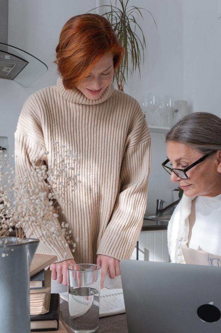 An adult daughter and her senior mother reviewing options together on a laptop in a bright kitchen