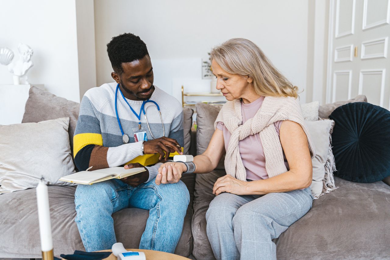 Healthcare coordinator visiting a senior woman at home, sitting together on a sofa reviewing health information