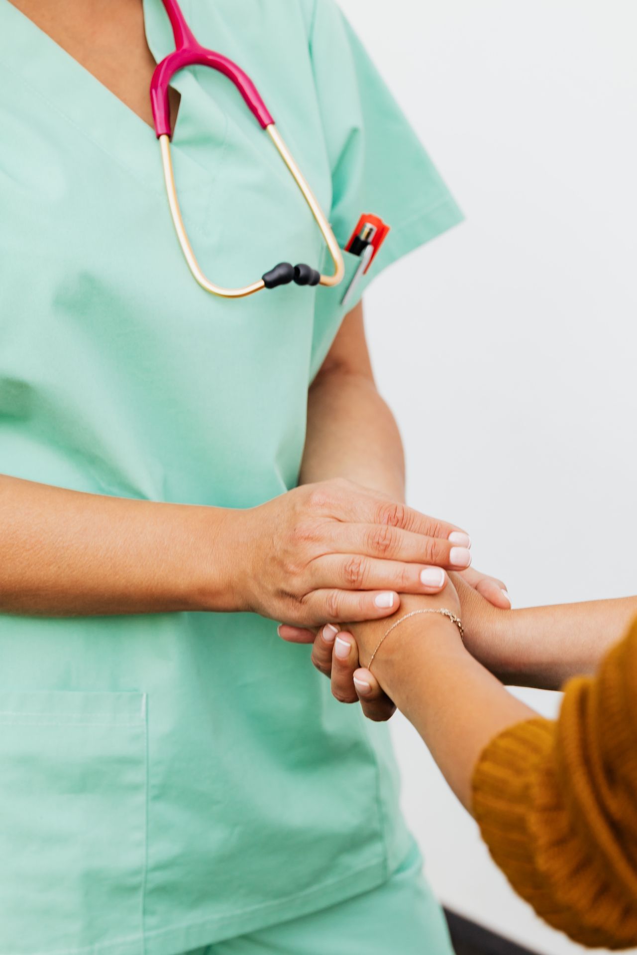 Caregiver in green scrubs compassionately holding patient hand in clinical setting