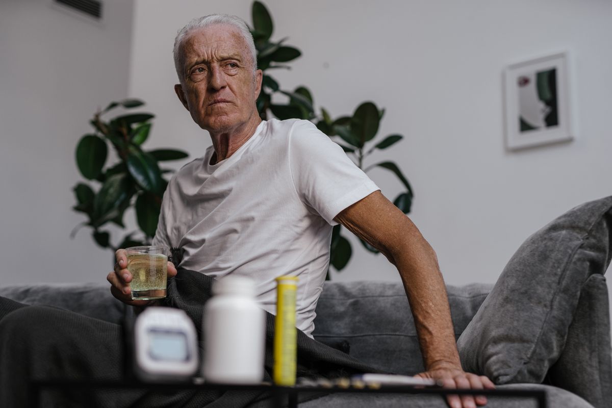 An older man drinking a glass of water at home next to his medication