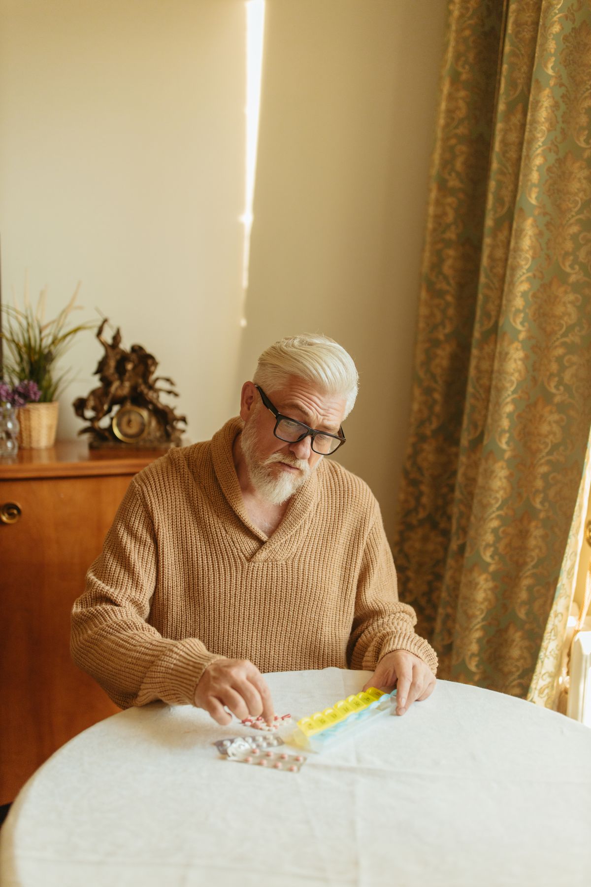 An older man reviewing his weekly pill organizer at home