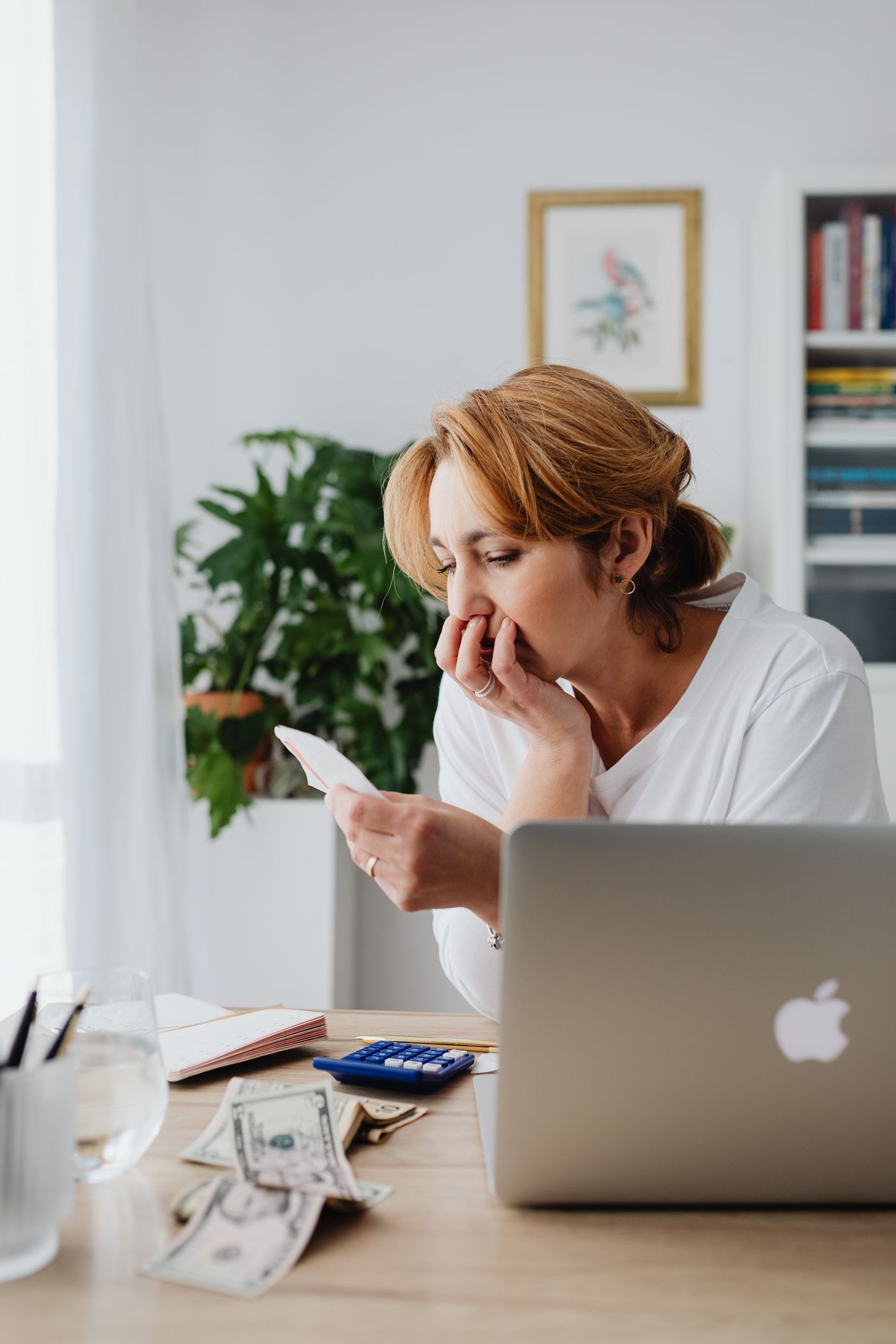 A woman reviewing home care bills with a calculator and laptop at her kitchen table