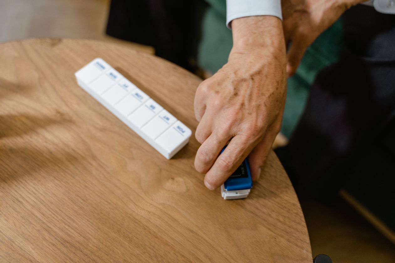 Elderly hand using a pulse oximeter next to a weekly pill organizer on a table