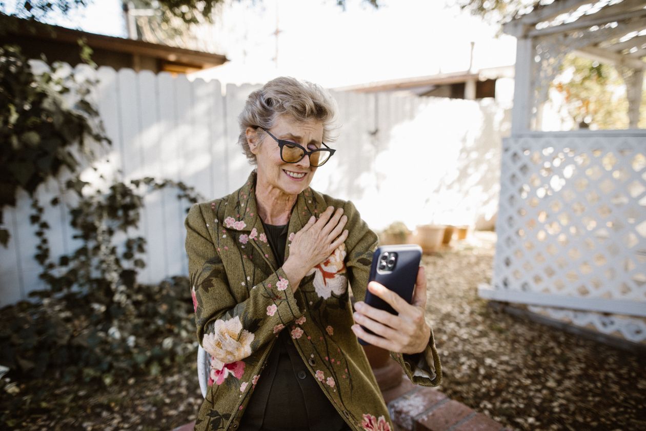 Senior woman smiling during a video call check-in with family from her backyard