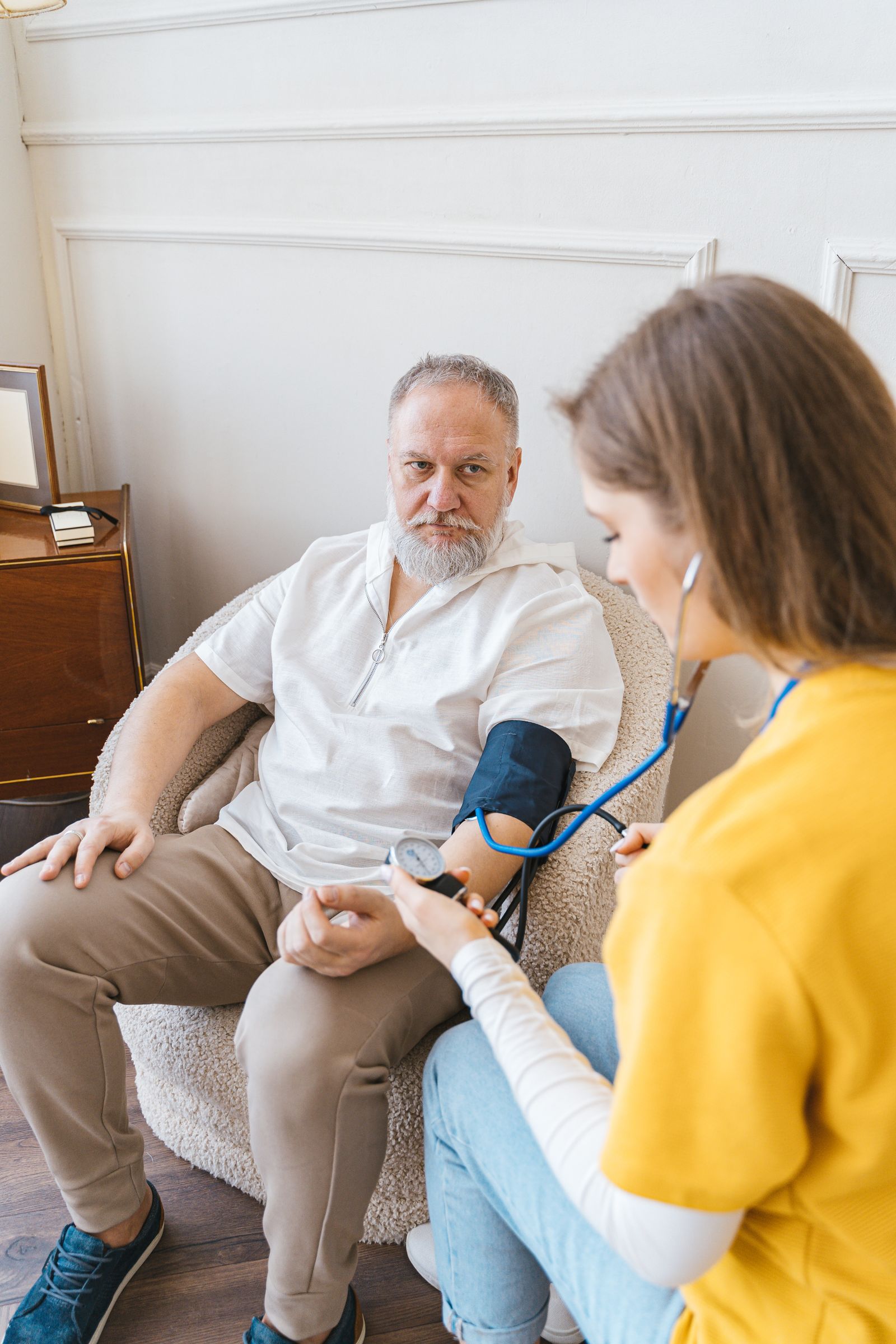 A caregiver checking an older man's blood pressure with a manual cuff in a home-like setting