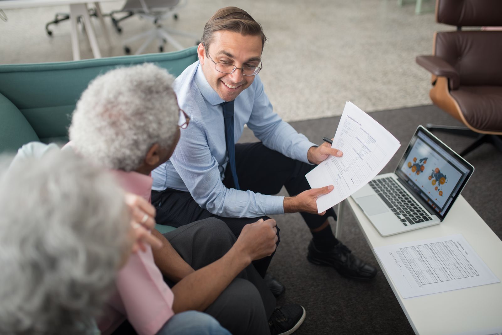 A counselor in business attire explains an application form to a senior client in an office setting