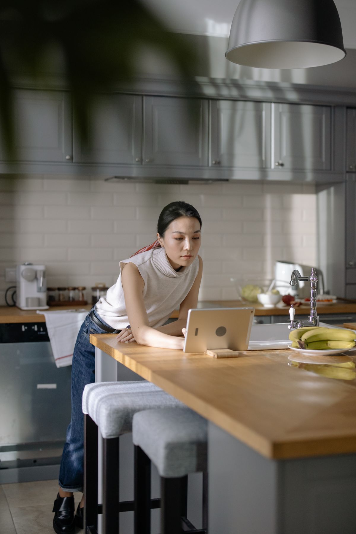 A woman leans on her kitchen counter reviewing records on a tablet at home