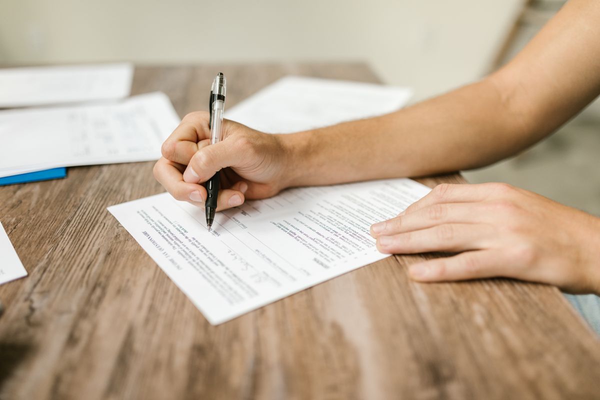 A close-up of a person's hands filling out a paper form at a wooden desk