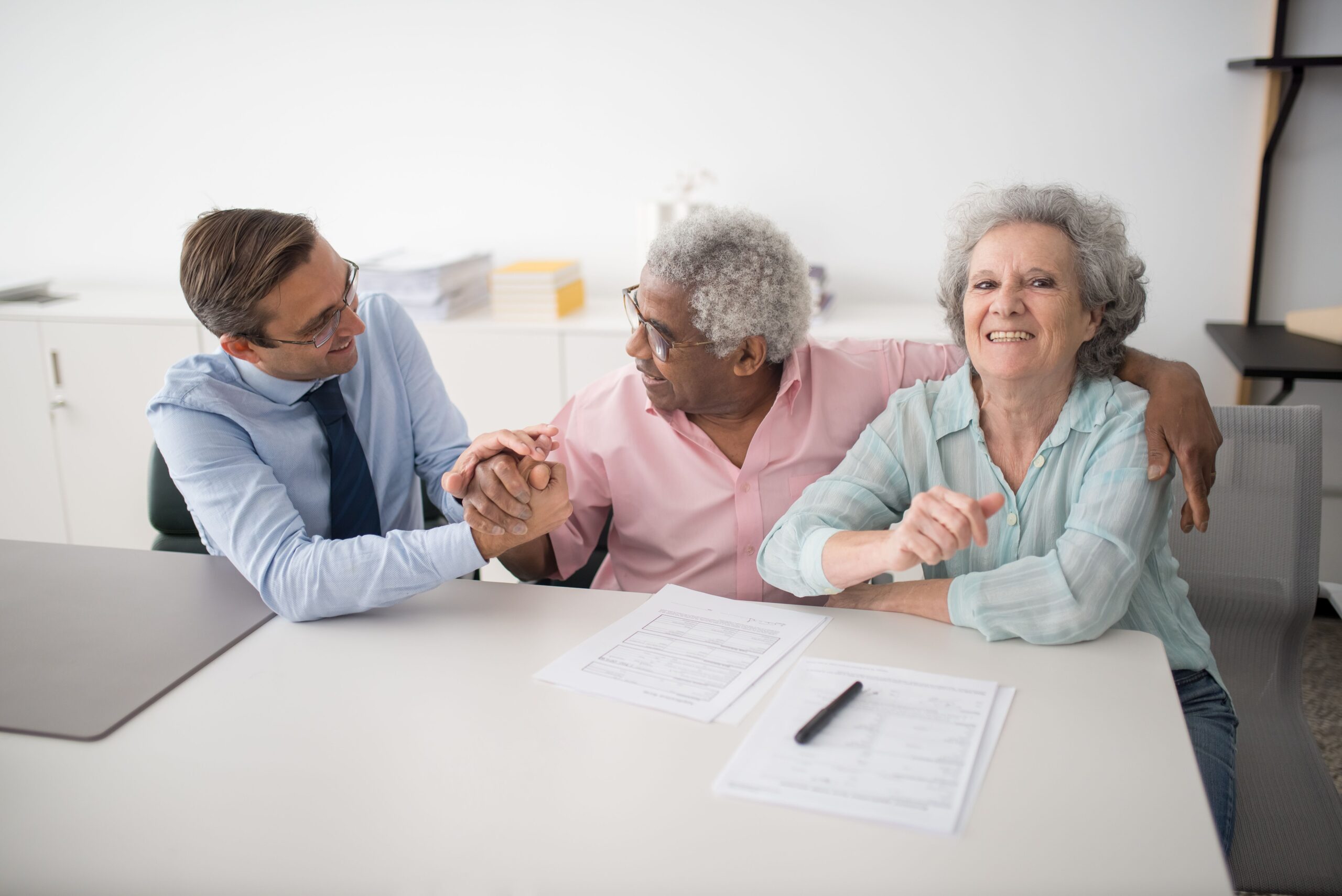 A senior couple shaking hands with an advisor across a desk covered in paperwork