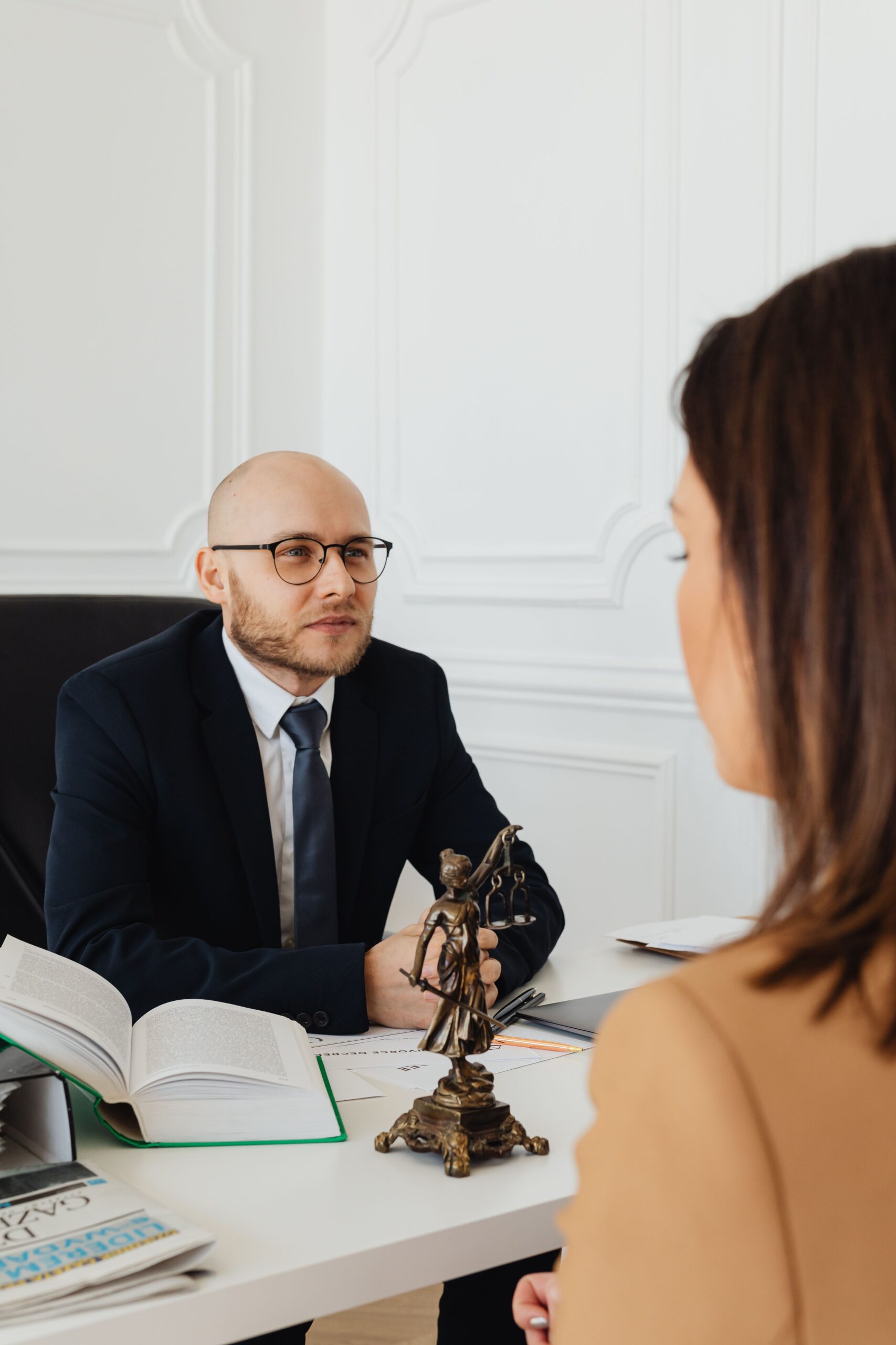 An attorney in an office consulting with a client, a small statue of the scales of justice on the desk