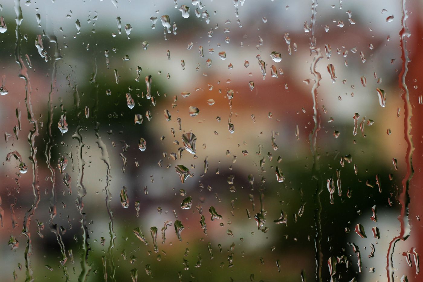 Raindrops running down a window pane with blurred houses beyond