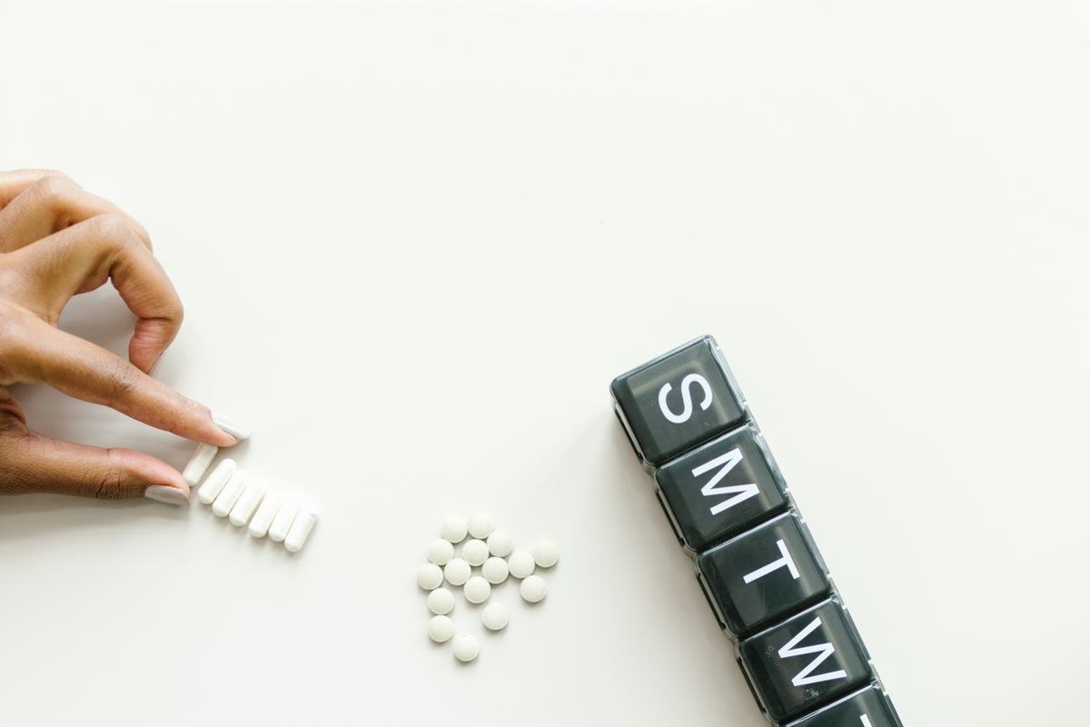 Older adult sorting tablets into a weekly pill organizer labeled Sunday through Saturday