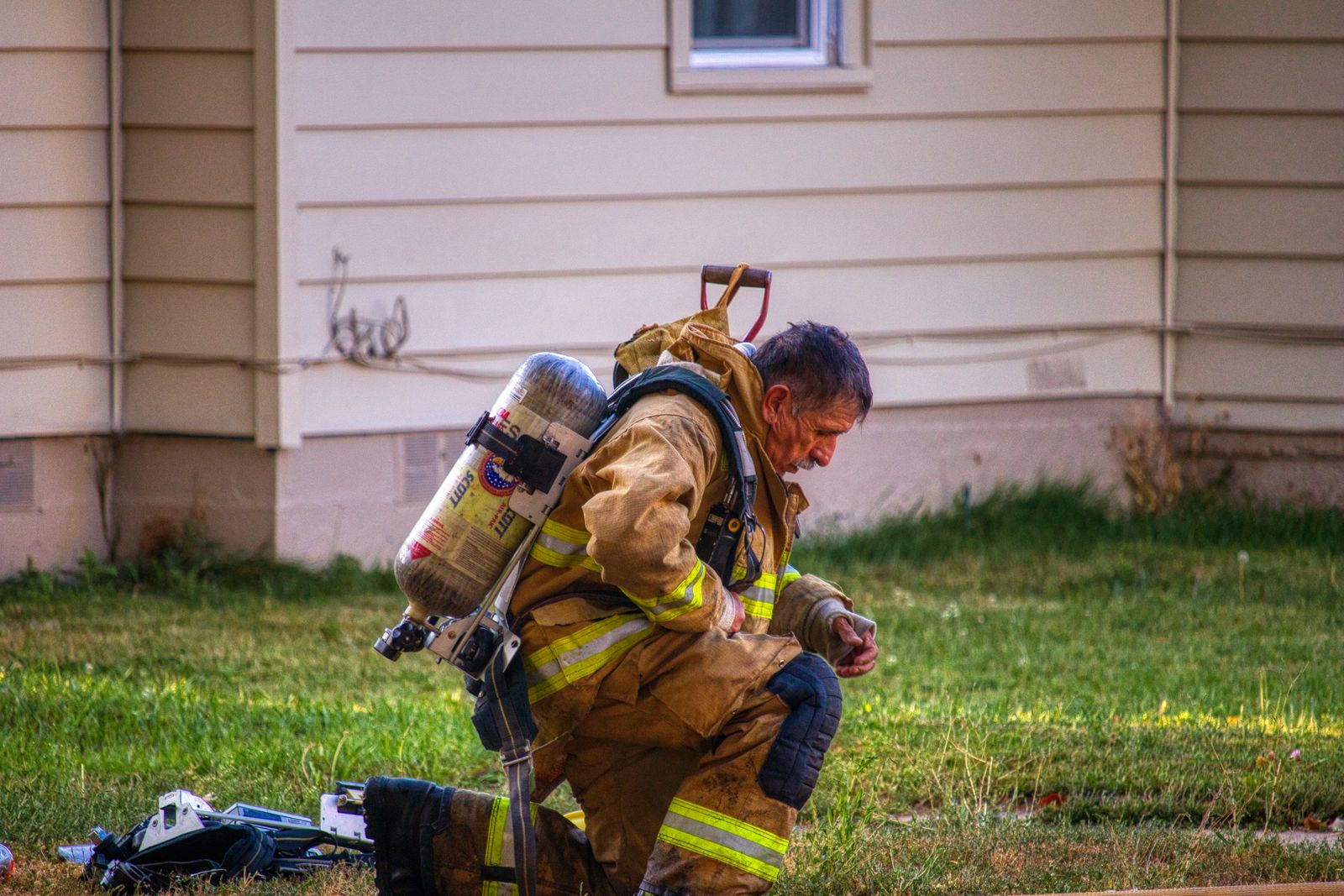 Firefighter in full turnout gear kneeling beside a house