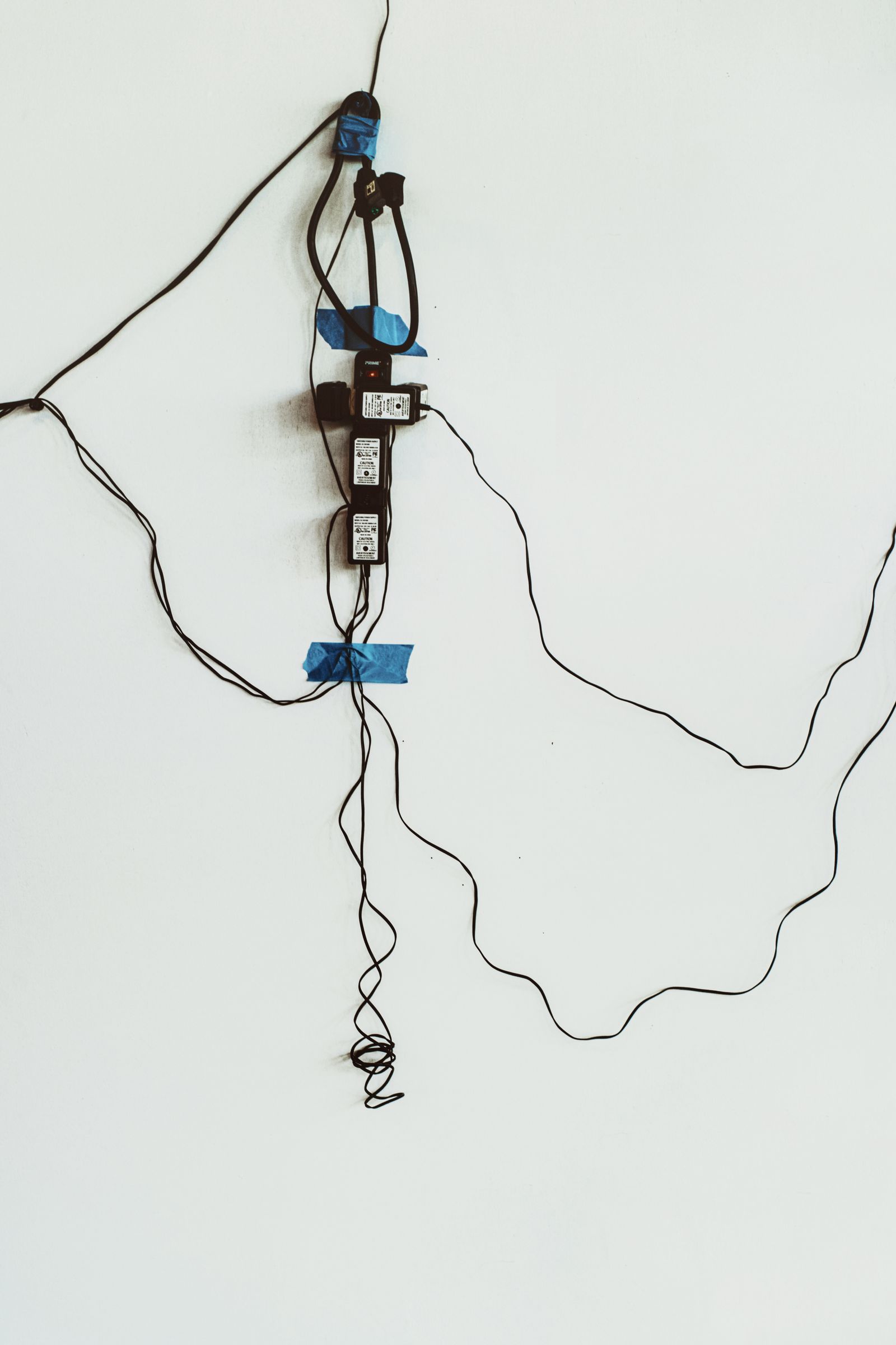 Tangled power cords and adapters taped along a wall