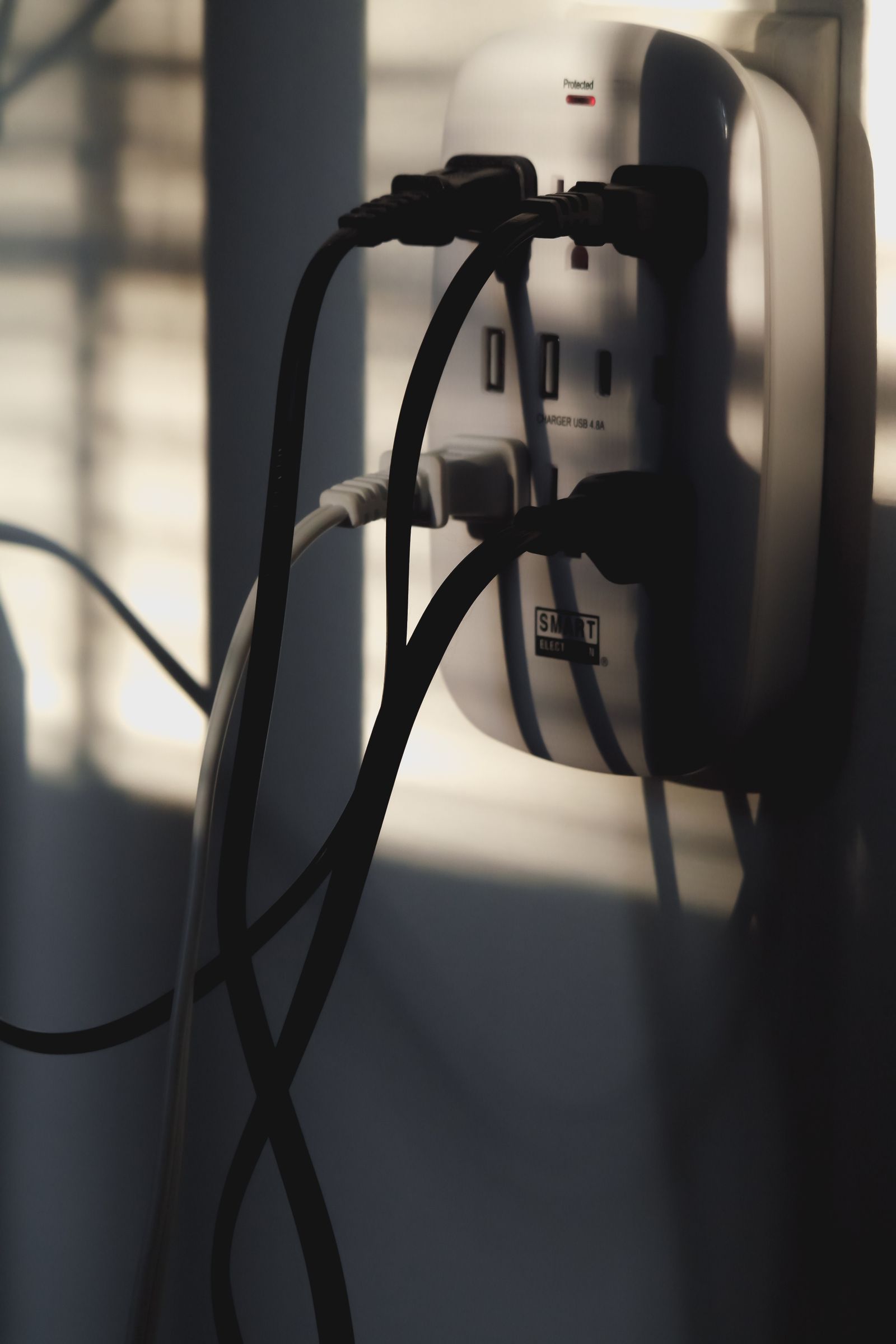 Multiple cords and chargers plugged into a single wall outlet with surge protector
