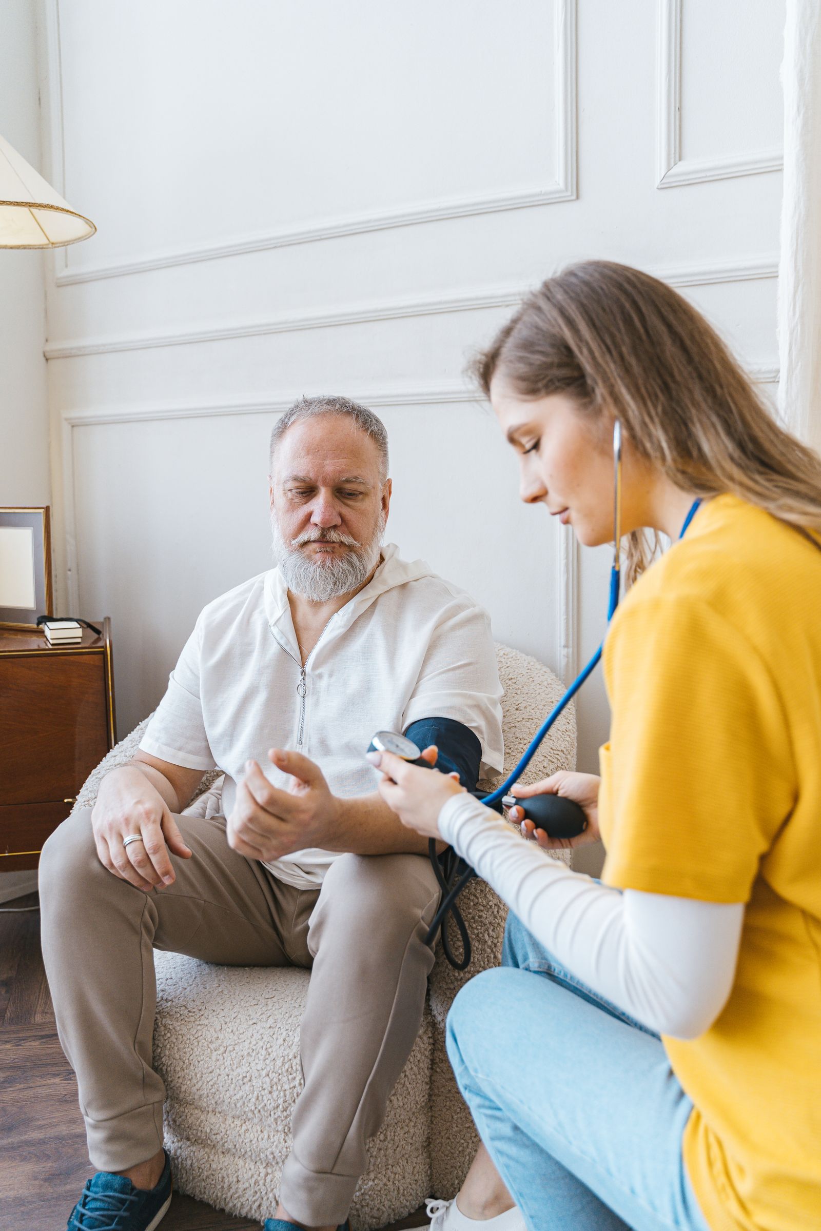A home health worker checks an older man's blood pressure during an in-home visit