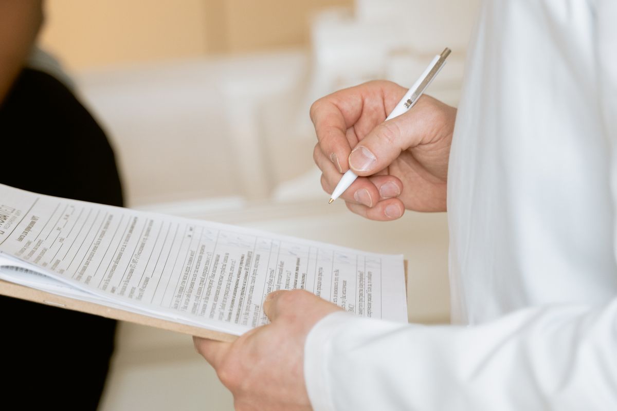 Clinician in a white coat reviewing a patient form on a clipboard