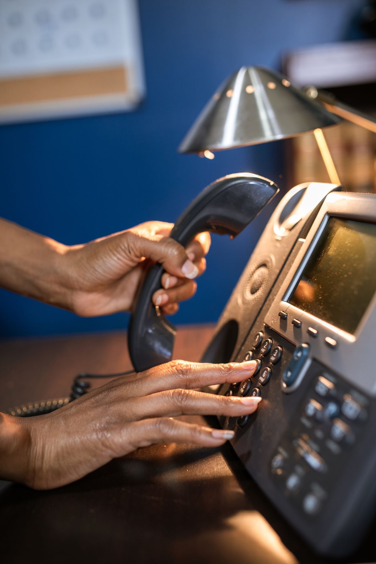 Hands dialing a desk telephone under a lamp