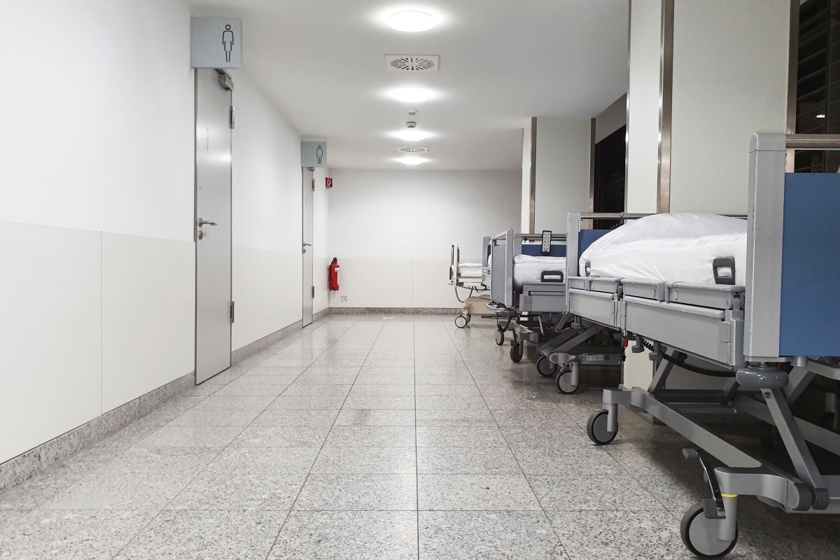 Empty hospital beds lined up along a bright hospital corridor