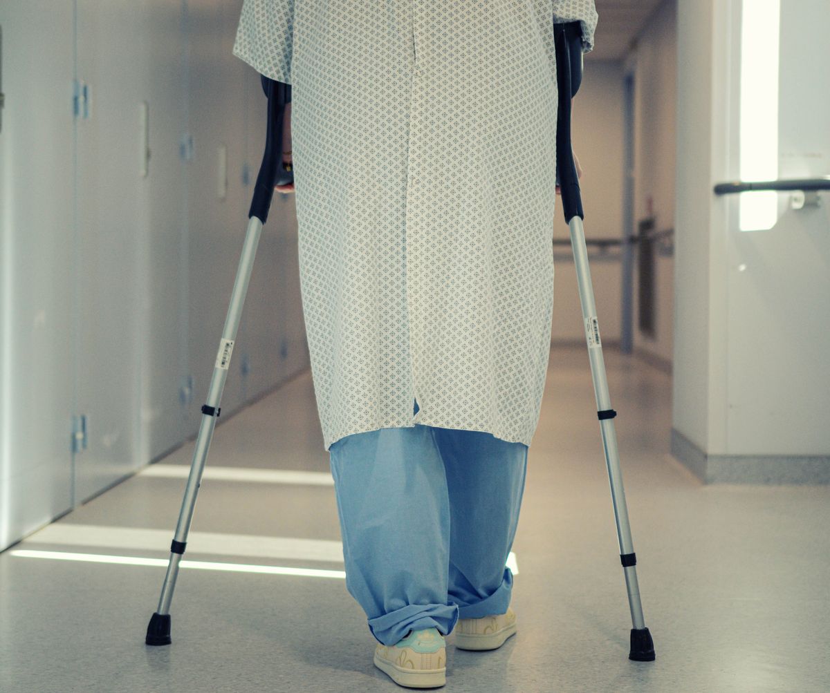 Patient in a hospital gown walking down a corridor on crutches