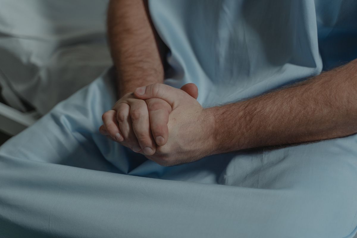 Hands of a hospital patient in a blue gown clasped together