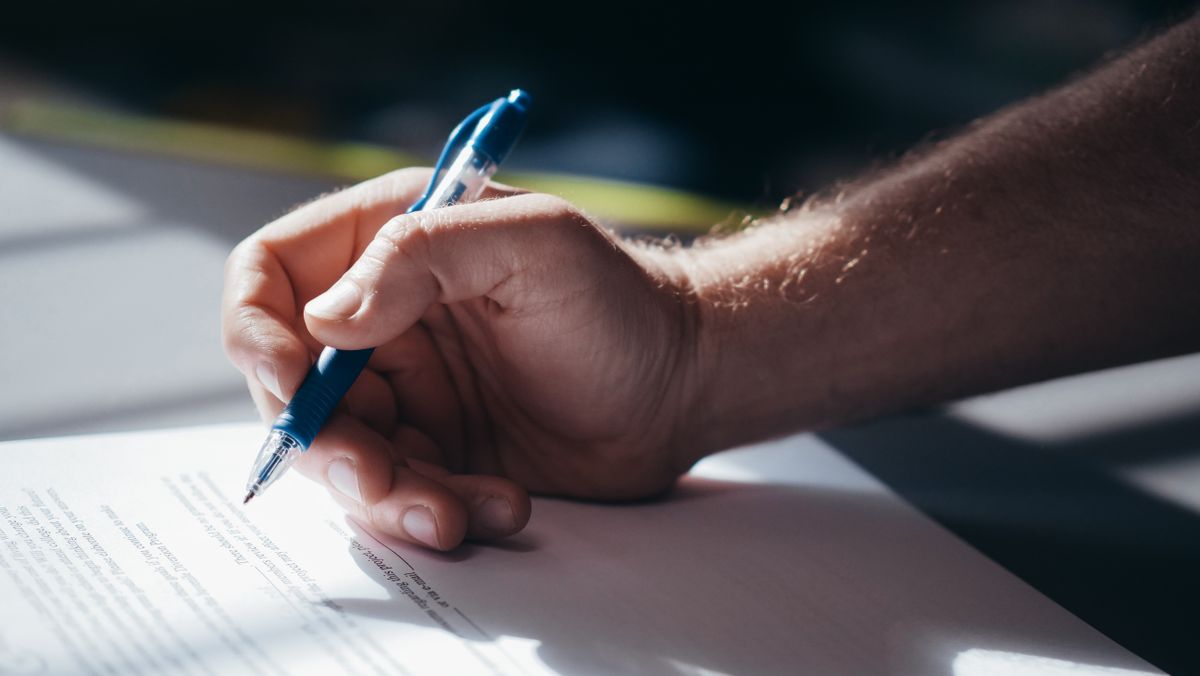 Hand signing a printed document with a blue pen