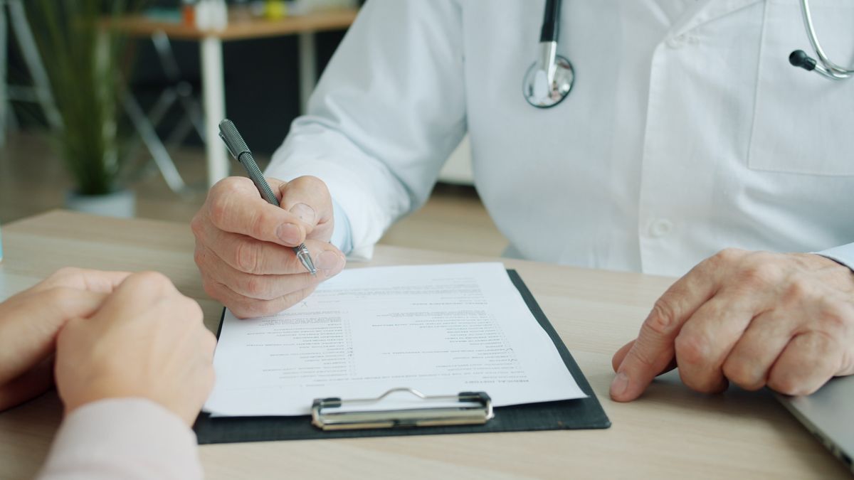 Clinician with a stethoscope reviewing a clipboard document with a patient