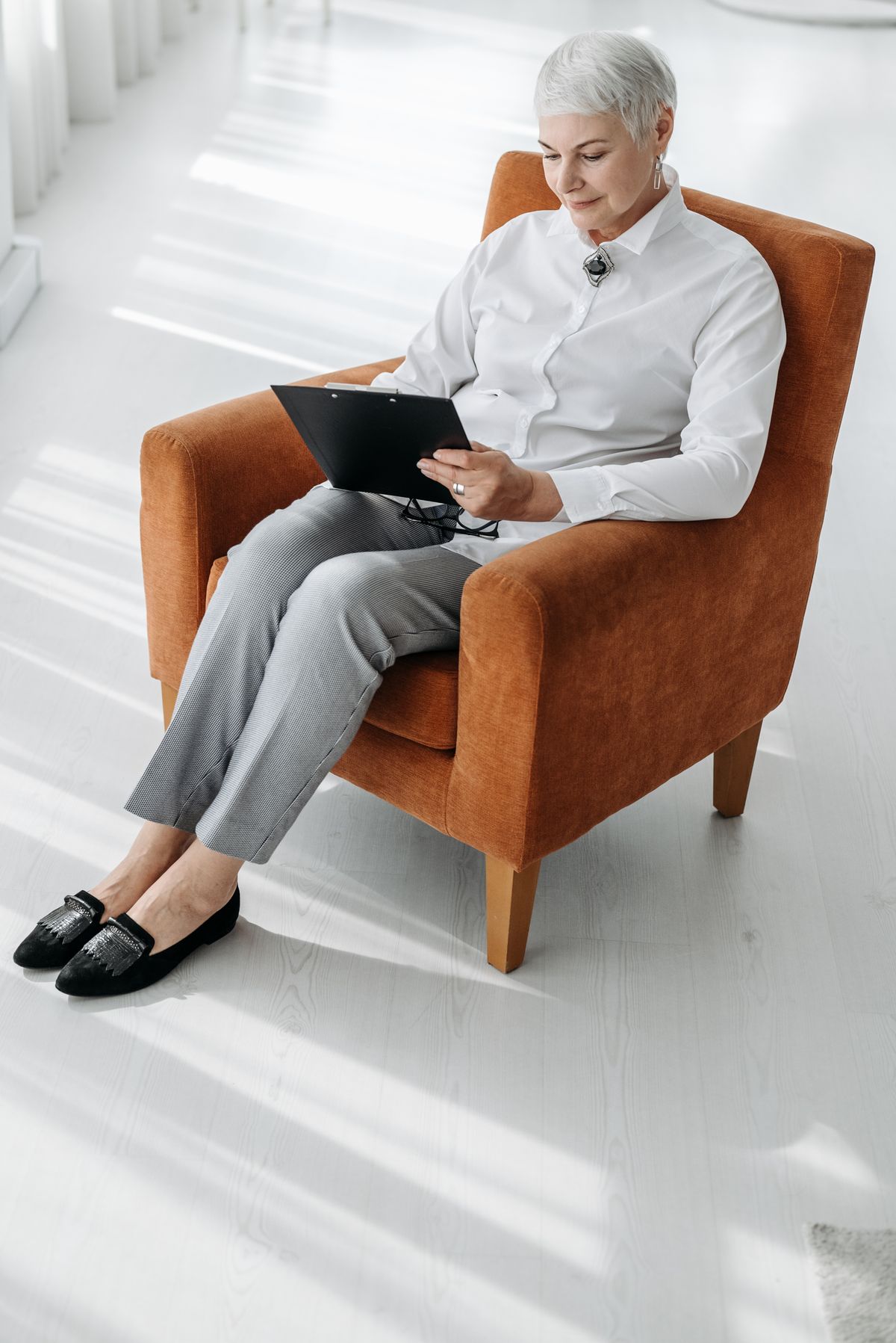 Older woman sitting in an armchair at home reviewing a clipboard document on her own