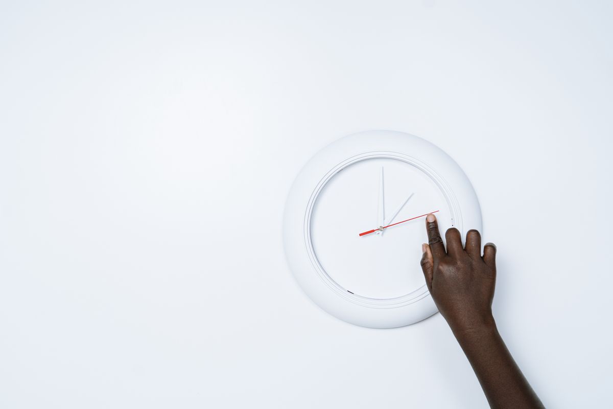 A hand adjusting a white wall clock, representing the daylight saving time change on November 1