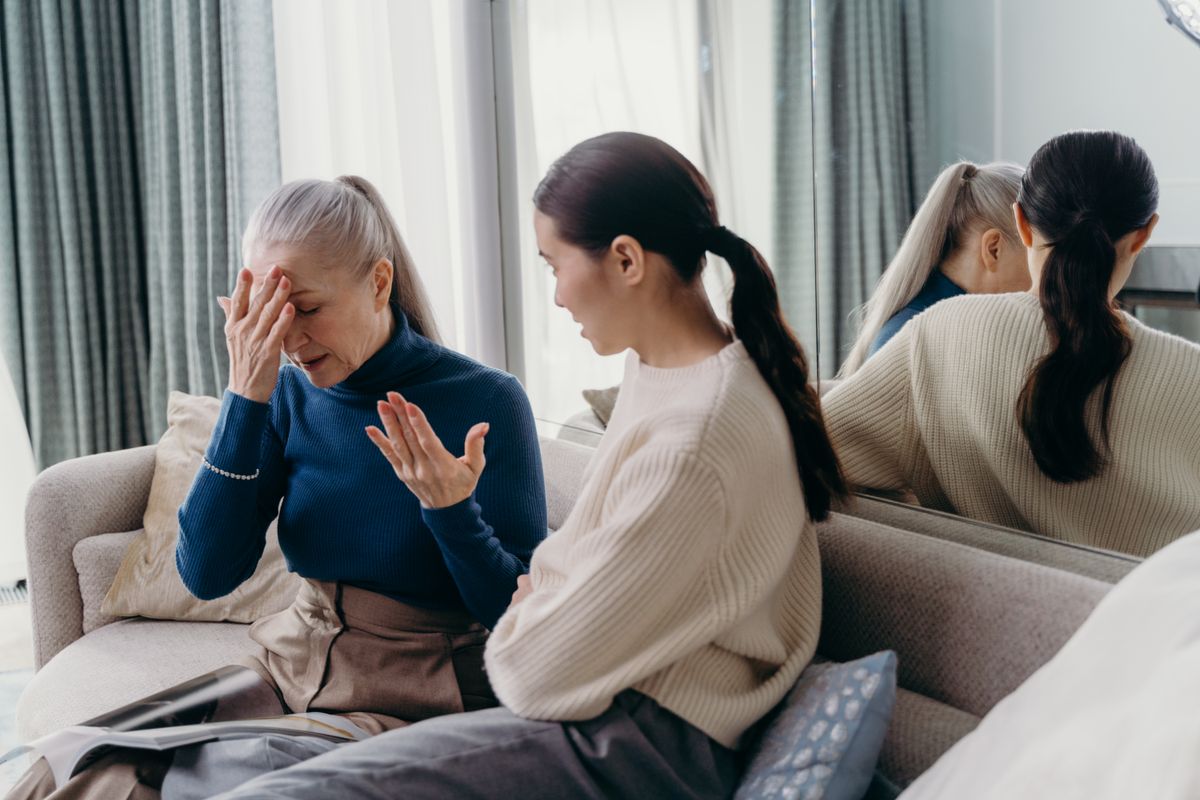 An adult daughter comforting her senior mother, who appears distressed, on a couch at home in the evening