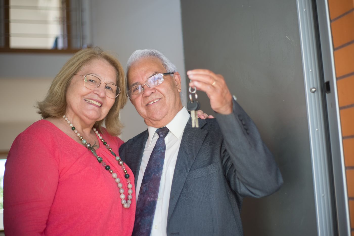 Smiling older couple standing in the doorway of their home holding a set of house keys