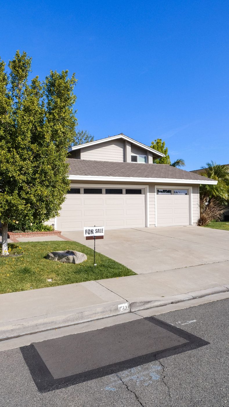 Two-story suburban home with a for sale sign on the front lawn under a clear blue sky