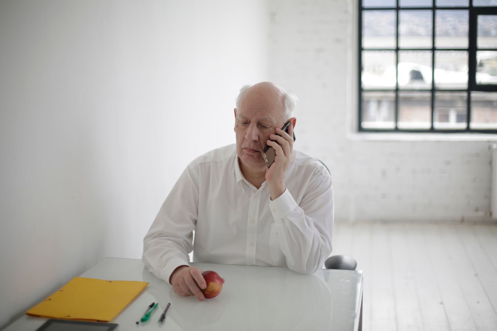 Older man in a white shirt seated at a desk, listening carefully during a phone call