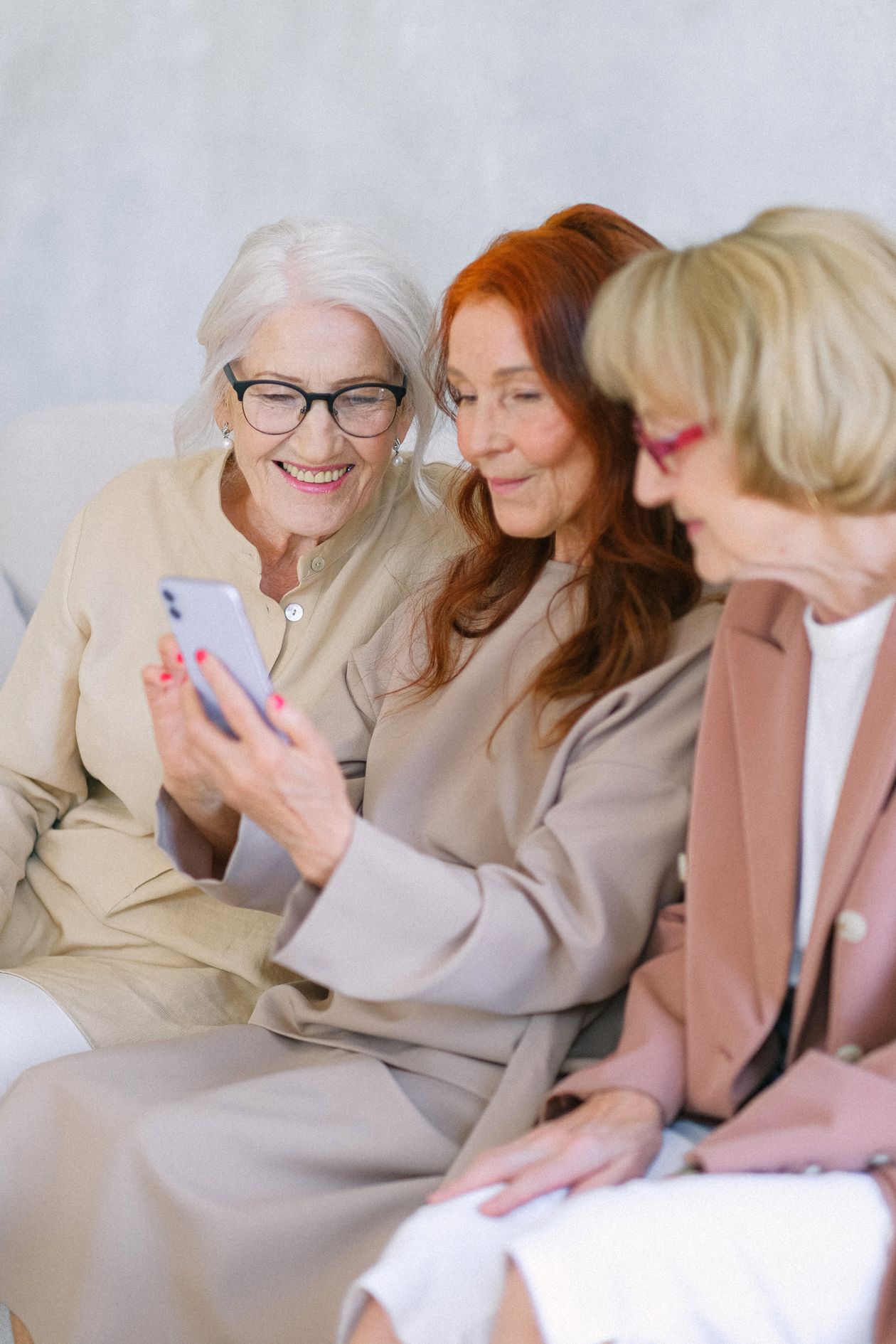 Three older women sitting together on a sofa smiling at a smartphone