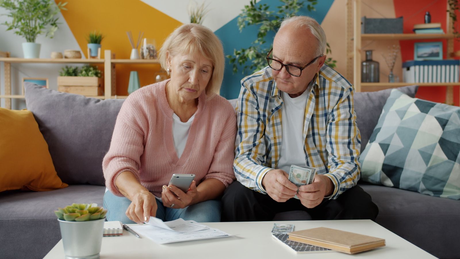 Older couple sitting on a sofa reviewing household bills and paperwork together
