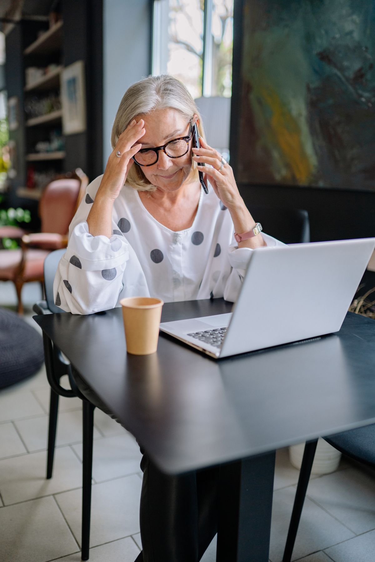 Older woman on the phone looking concerned while sitting at a laptop