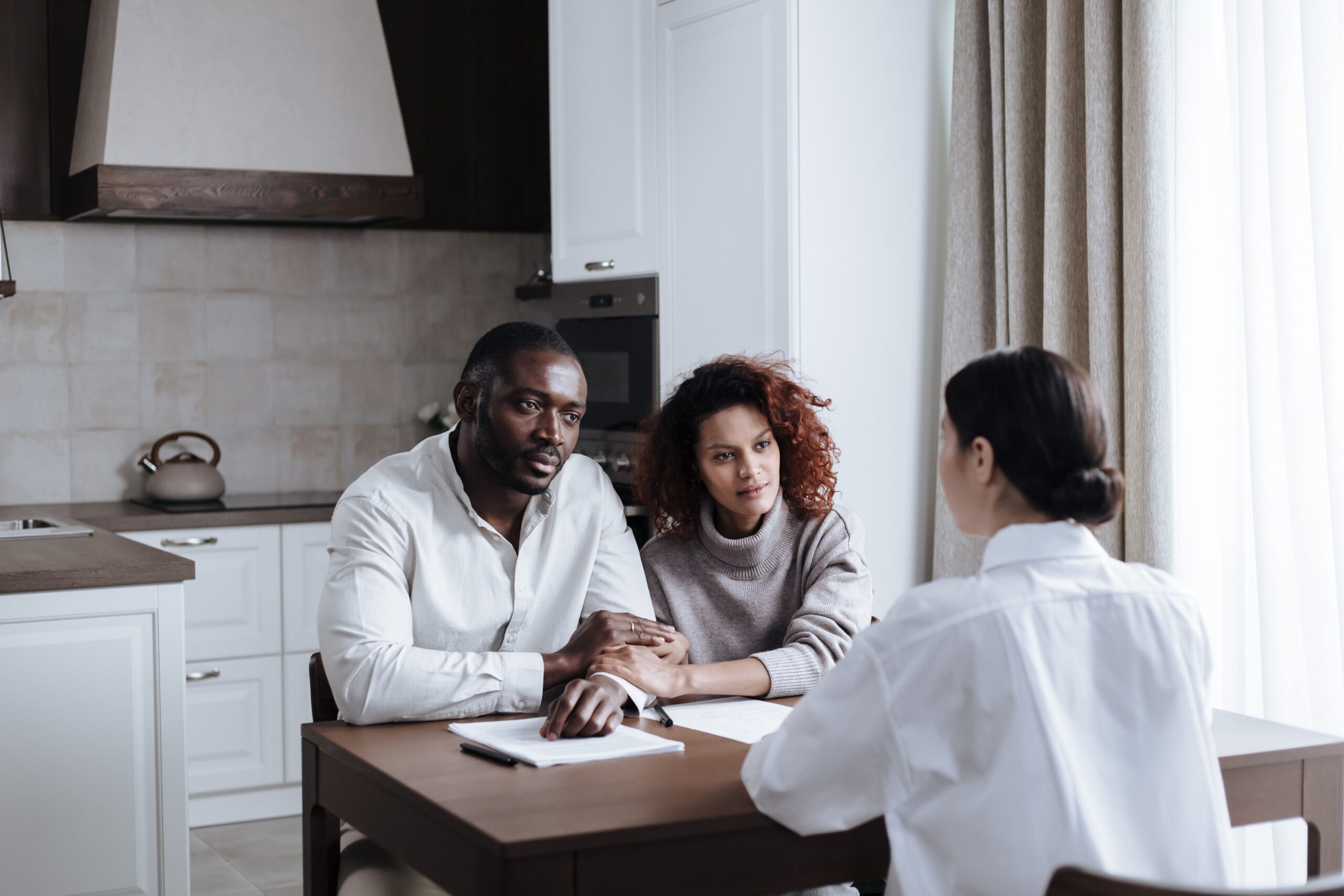 Adult couple sitting at a kitchen table reviewing documents with a professional advisor