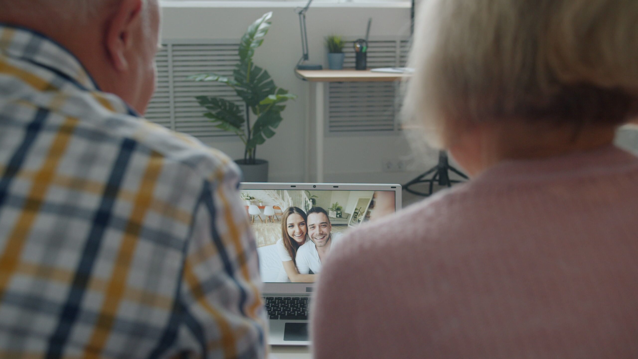 Senior couple on a video call with their adult children, who appear happy and relaxed on the laptop screen